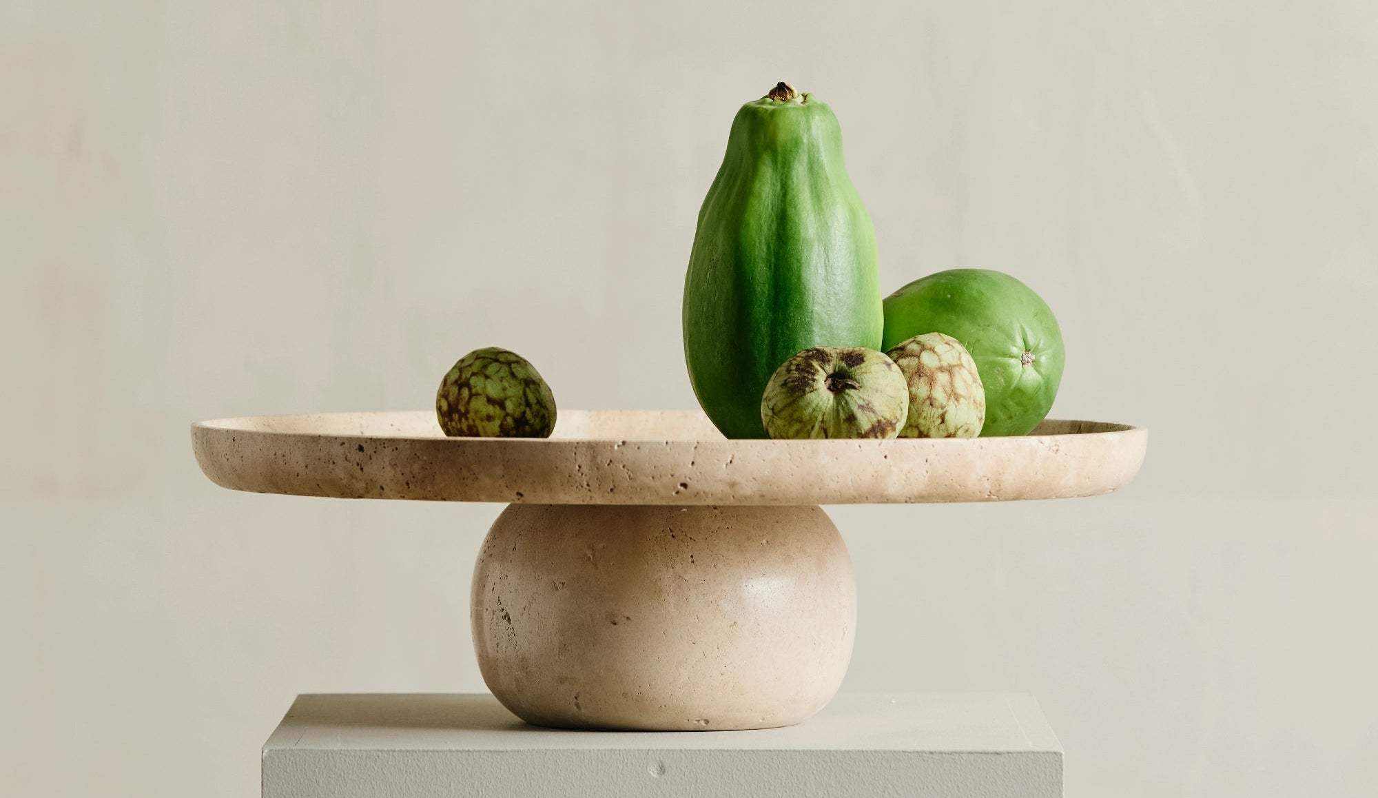 Decorative stone pedestal with green fruits on a neutral background